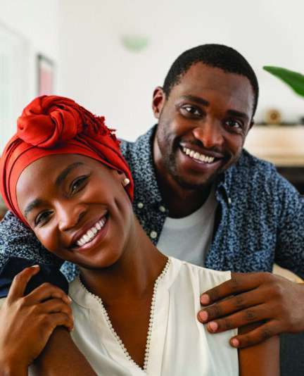 Portrait,Of,Mid,Adult,Happy,African,American,Couple,Hugging,At Portrait of mid adult happy african american couple hugging at home while sitting on couch. Portrait of mature man with his woman wearing traditional turban looking at camera. Black mid adult couple.